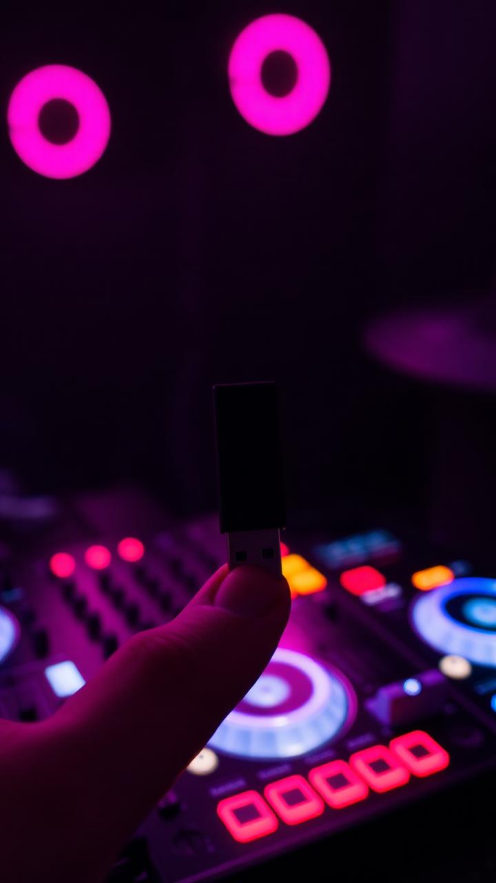 A USB stick held up in front of a glowing DJ controller